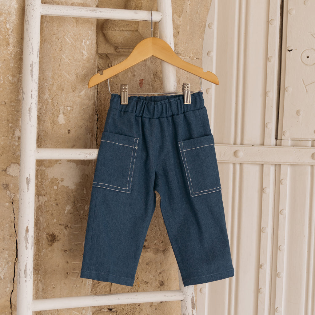 Blue recycled denim  childrens unisex jeans with elasticated waist and large pockets on the hip with contrast white stitching hanging from a ladder